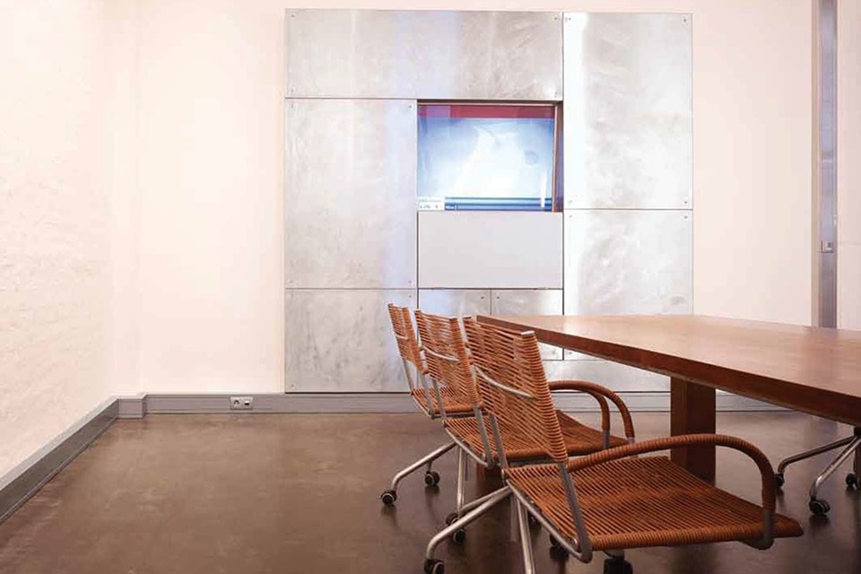 Sala de reuniones moderna de oficina con caja eléctrica metálica de suelo, mesa grande y sillas de mimbre