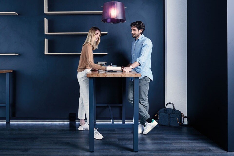 Dos personas trabajando en escritorios de pie en un entorno de oficina moderno con iluminación LED