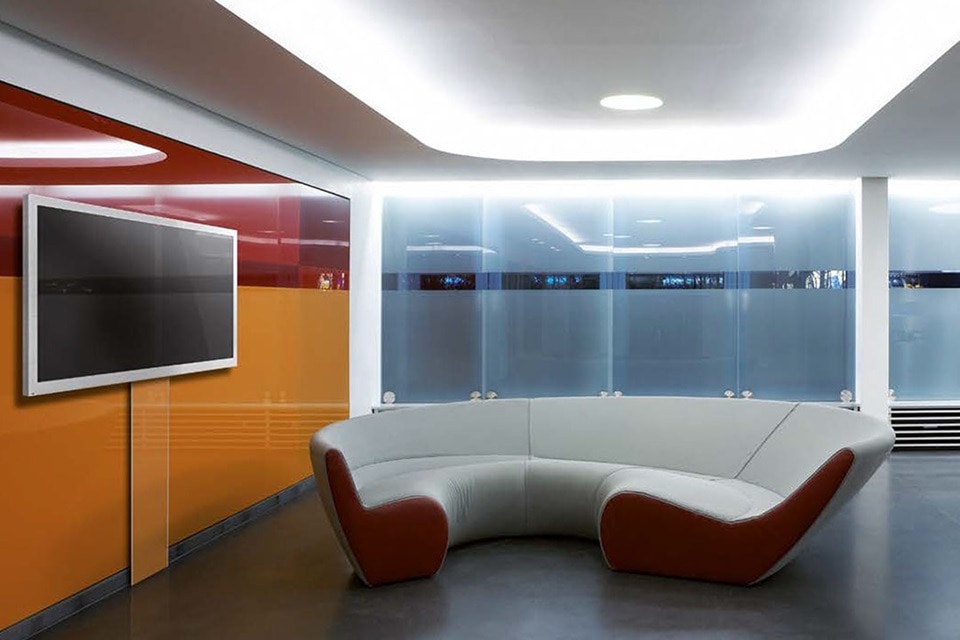 Vestíbulo de oficina moderno con sofá curvo y televisor de pantalla plana en la pared, iluminado por luces empotradas en el techo