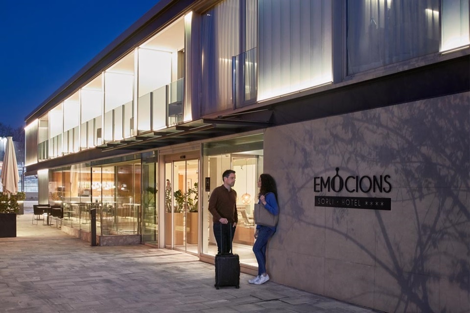 Vue extérieure d'un bâtiment hôtelier moderne au crépuscule avec façade éclairée et clients avec bagages