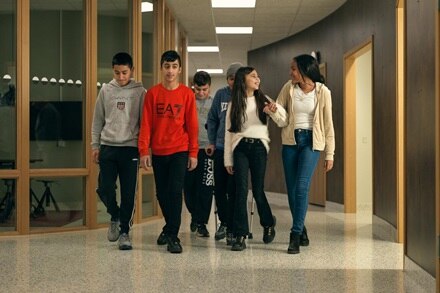 Six personnes traversent un couloir moderne avec des éléments en bois et en verre, habillées de manière informelle et apparemment engagées dans une conversation.