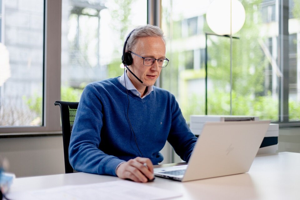 personne assise à son bureau avec un ordinateur portable devant lui et des écouteurs sur les oreilles