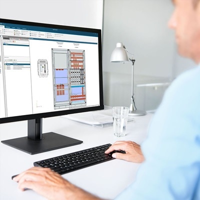 Cette photo montre une personne travaillant à un bureau avec un écran d'ordinateur affichant une interface logicielle Hager. L'interface affiche des données et des paramètres liés à l'ingénierie électrique ou à la configuration du système. Une lampe de bureau est placée sur le bureau.