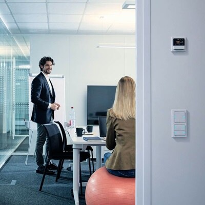 homme et femme dans salle de réunion et interrupteurs KNX contre le mur