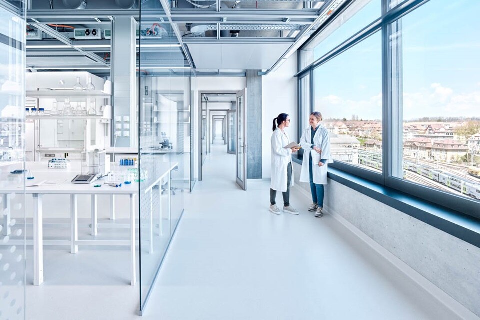 Deux professionnels en discussion dans un laboratoire moderne avec des conduits électriques visibles au plafond