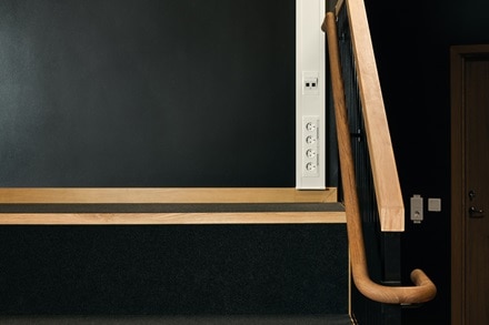 Espace intérieur avec rampe en bois et mur blanc avec plusieurs prises et un interrupteur, dans un intérieur moderne.