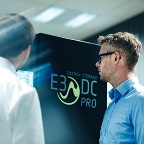Deux personnes se tiennent devant un système de stockage d’énergie étiqueté « E3DC PRO » et marqué « ENERGY STORAGE » dans un cadre professionnel.