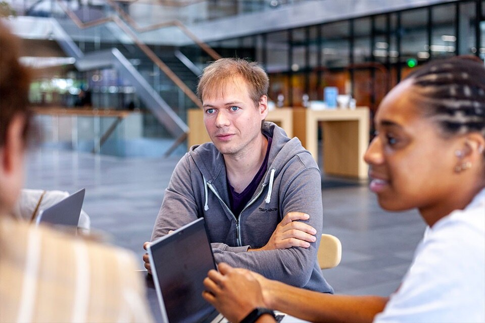 Un groupe de personnes se réunissant autour d'une table dans un espace de bureau ouvert moderne avec lumière naturelle.