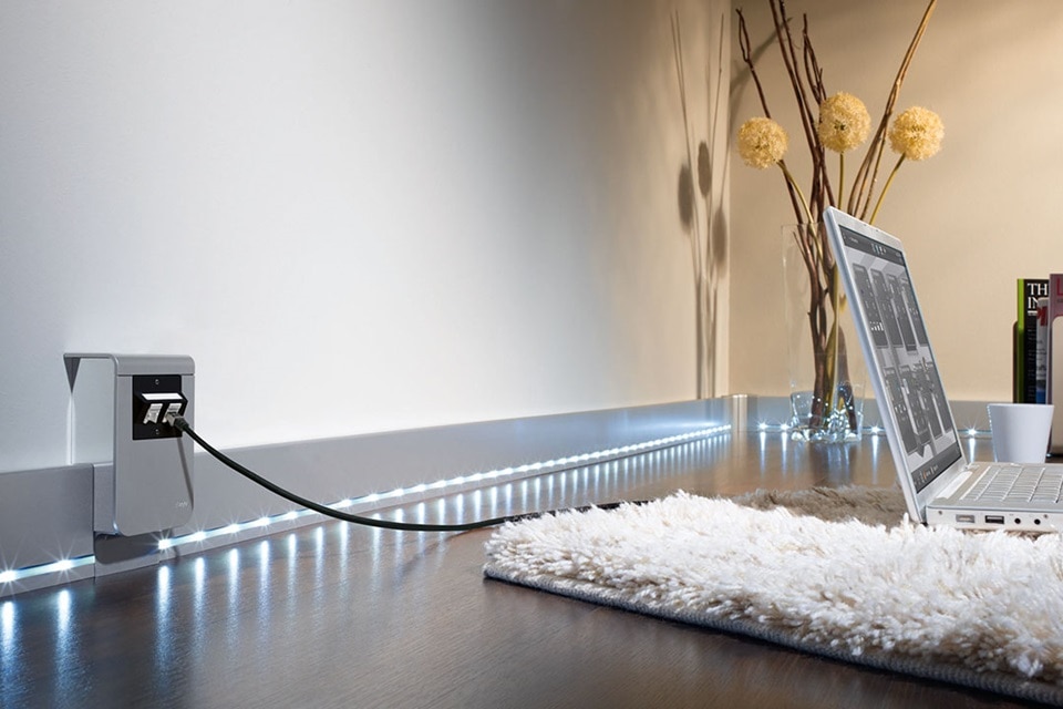 Intérieur résidentiel moderne avec éclairage de plinthe LED et prise électrique murale avec ports USB chargeant un ordinateur portable