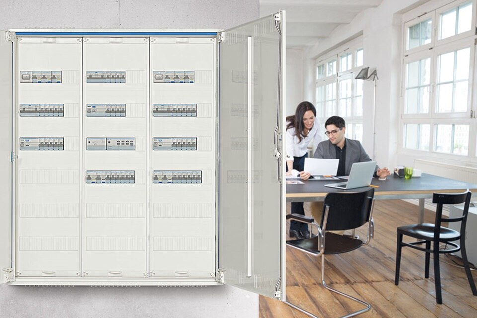 Tableau de distribution électrique dans un environnement de bureau avec deux personnes discutant d'un projet