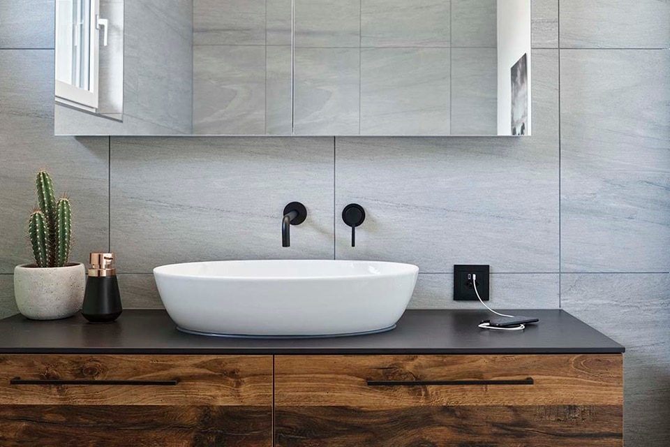 Intérieur de salle de bain moderne avec lavabo mural, robinets noirs mats et prise électrique près du plan de travail en bois.