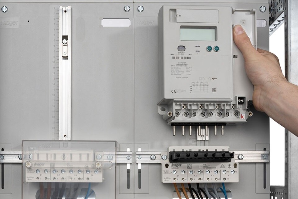 Personne installant un compteur d'énergie Hager dans un tableau électrique, à côté de disjoncteurs et d'accessoires de câblage
