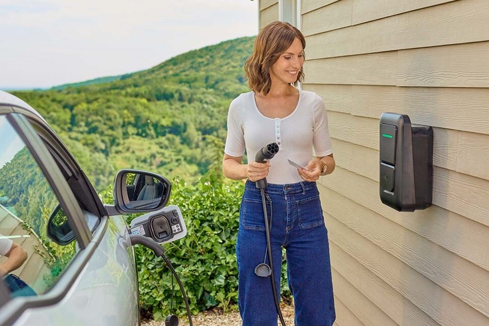 Une femme recharge sa voiture électrique chez elle avec la borne de recharge witty one de Hager.
