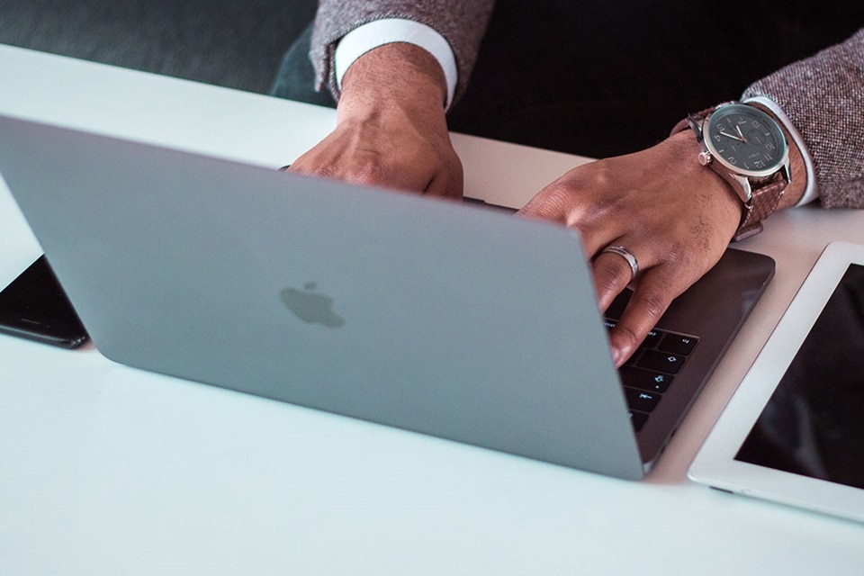 Personne utilisant un ordinateur portable avec un smartphone et une montre connectée visibles sur un bureau