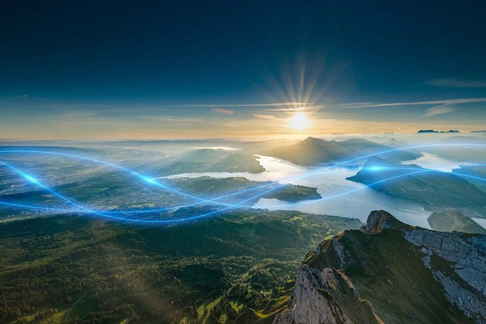 Lever de soleil sur un paysage montagneux avec des ondes énergétiques bleues symbolisant la distribution d'énergie électrique
