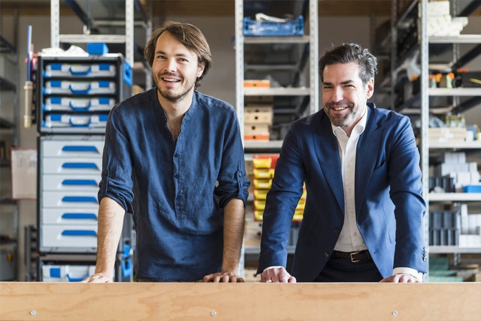 Deux personnes souriantes dans un entrepôt avec des composants électriques en arrière-plan