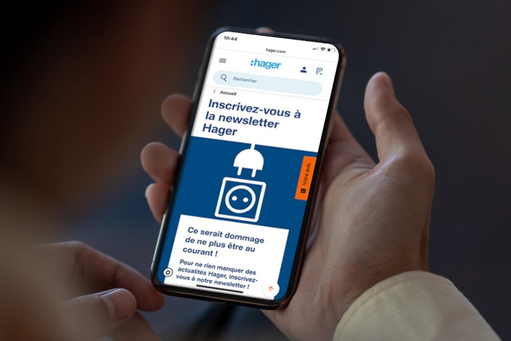 Personne tenant son smartphone affichant la newsletter qui informe de la disponibilité du guide de la nouvelle NF C 15-100 de Hager