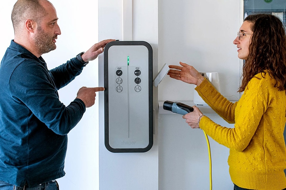 couple discutant autour de leur borne de recharge witty de Hager posée au mur dans leur garage