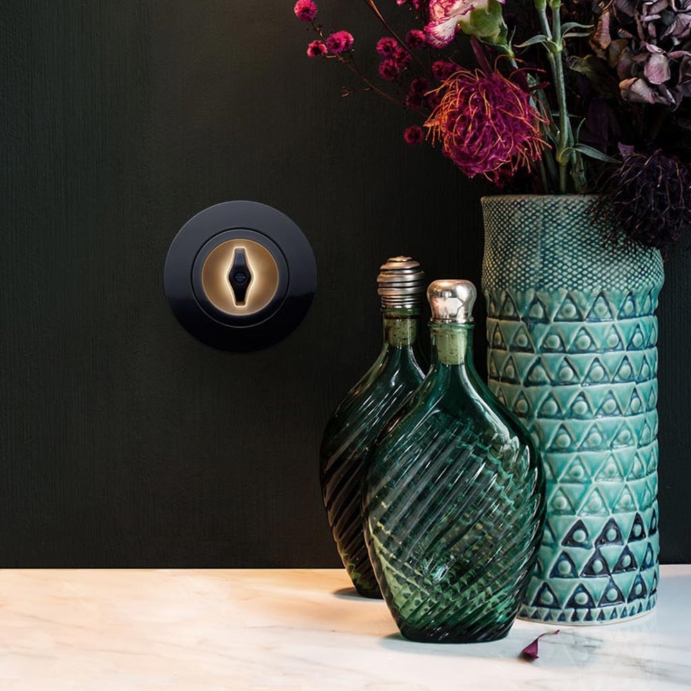 interrupteur lumineux noir 1930 derrière une table avec un vase et des flacons en verres vert