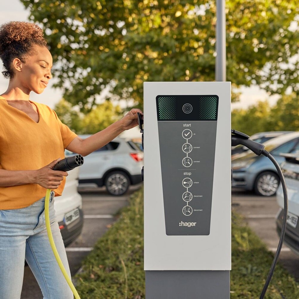 Jeune femme qui recharge un véhicule électrique grâce à une borne de recharge witty park de Hager sur un parking d'entreprise