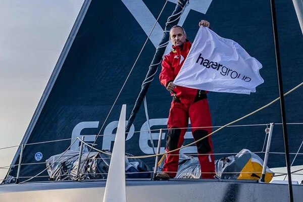 Le skipper Fabrice Amedeo sur son bateau, en mer,  tenant le drapeau Hagergroup