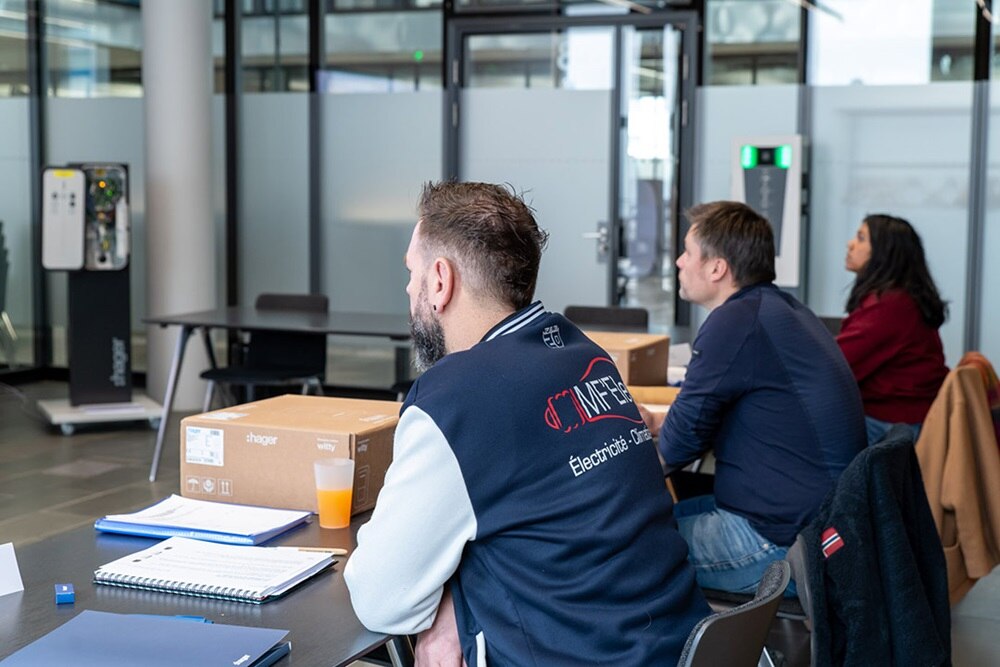 Une femme et deux hommes qui apprennent à installer et configurer une borne de recharge witty de Hager