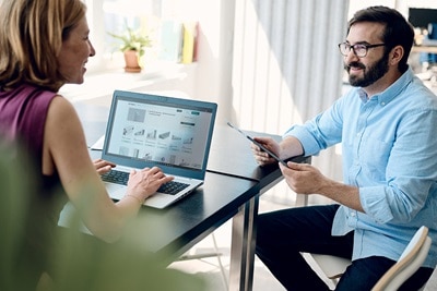 homme avec tablette face à une femme au bureau devant PC utilisant hagercad.T, logiciel qui exporte la modelisation des donnees du batiment (BIM)