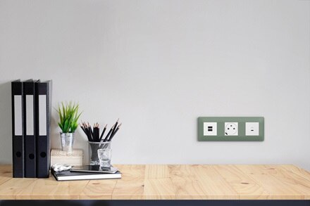 plaques 3 postes essensya botanic de Hager, 2 prises de courant affleurantes et prises USB-C sur un mur devant un plan de travail en bois clair, classeurs noirs et nécessaire de bureau