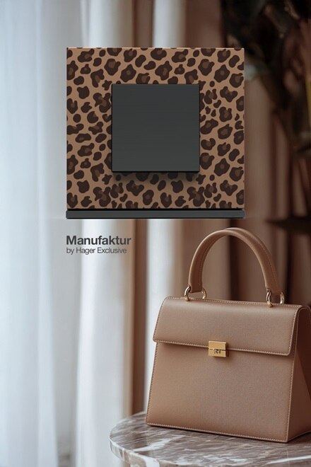 Interrupteur gallery personnalisé par Manufaktur by Hager Exclusive, motif léopard en arrière plan un sac de marque beige posé sur un guéridon en marbre et rideau beige rosé