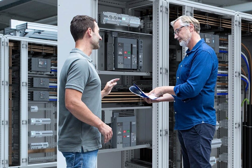 2 hommes en discussion devant une armoire quadro evo de Hager contenant des disjoncteurs ouverts hw+ de Hager