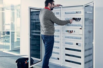 Electricien en train de manipuler une armoire quadro5 de Hager installée à l'entrée de bureaux d'entreprises