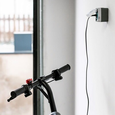 Prise witty de Hager pour les trottinettes, vélos, scooters et autos, trottinette branchée dans un garage, vue de l'intérieur sur le portail