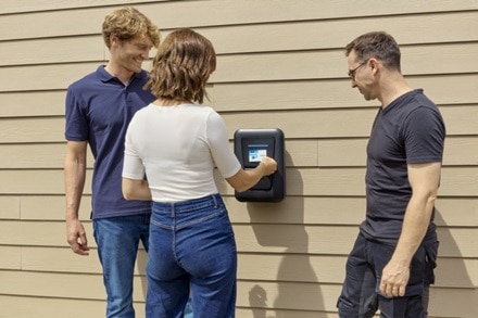 Installateur agréé IRVE qui explique à un couple comment utiliser une borne de recharge witty one version noire de Hager posée sur le mur de la maison