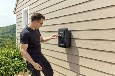 Homme ouvrant la trappe de la prise de la borne de recharge witty one version noire de Hager posée sur le mur de sa maison