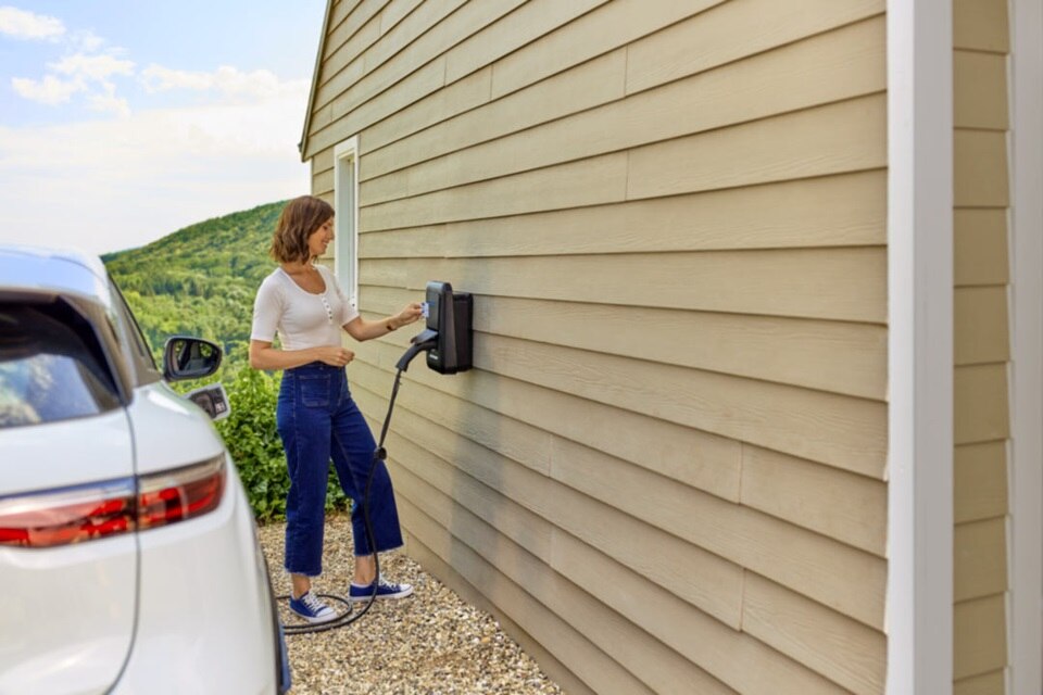 Femme qui charge son véhicule électrique avec une borne de recharge witty one de Hager posée sur le mur de sa maison