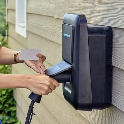 Main d'une femme qui branche une prise sur la borne de recharge witty one de Hager et qui tient un badge Hager