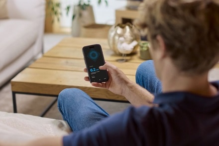 Homme assis sur son canapé utilisant l'app Hager Charge pour utiliser sa borne de recharge wittyone de Hager