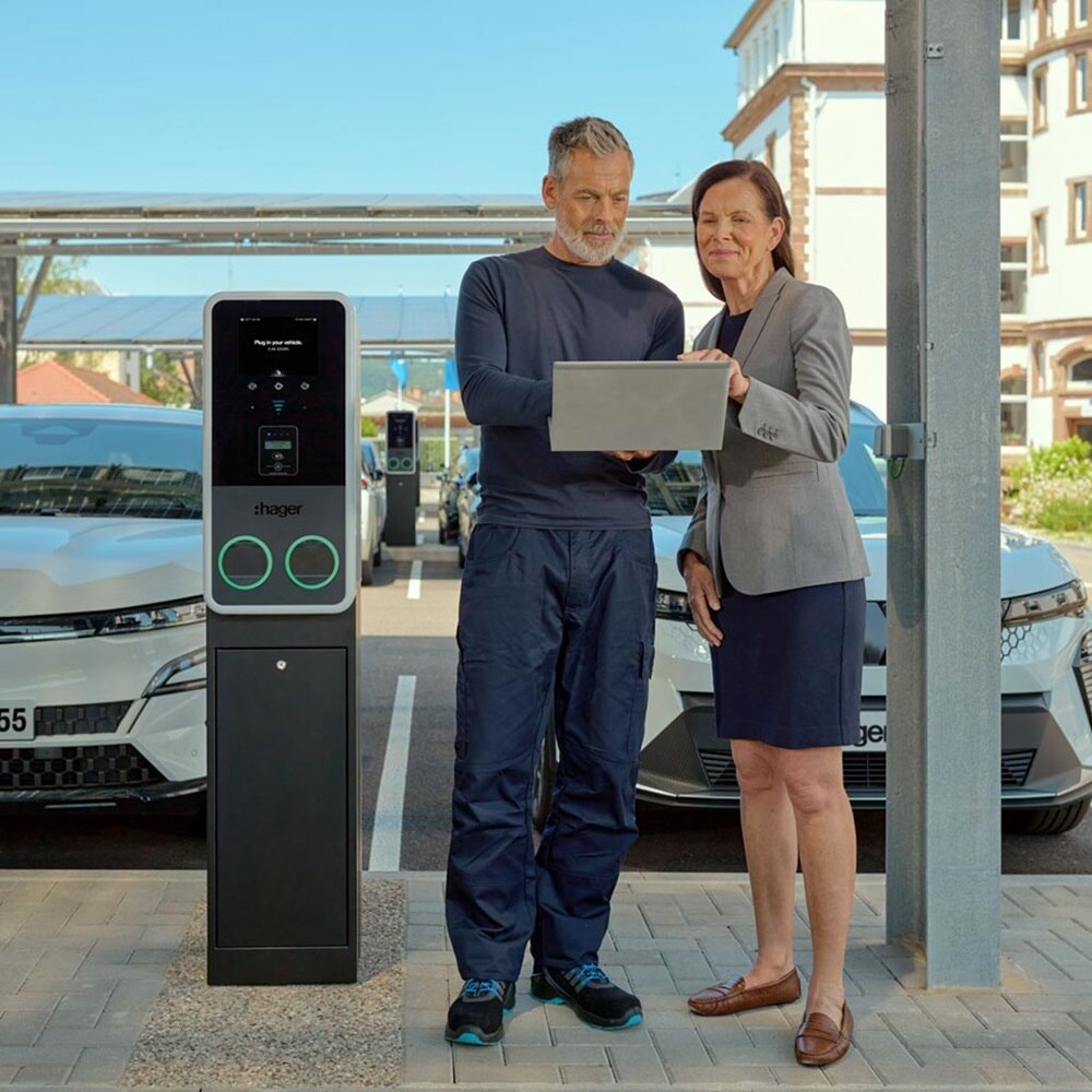Sur un parking doté de bornes de recharge witty park 2 de Hager, un couple optimise la performance énergétique du parc de bornes de recharge via un ordinateur.