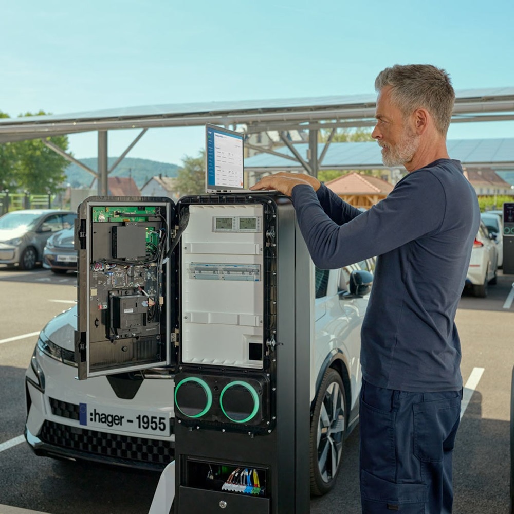Un homme installe une borne de recharge witty park 2 de Hager sur un parking.