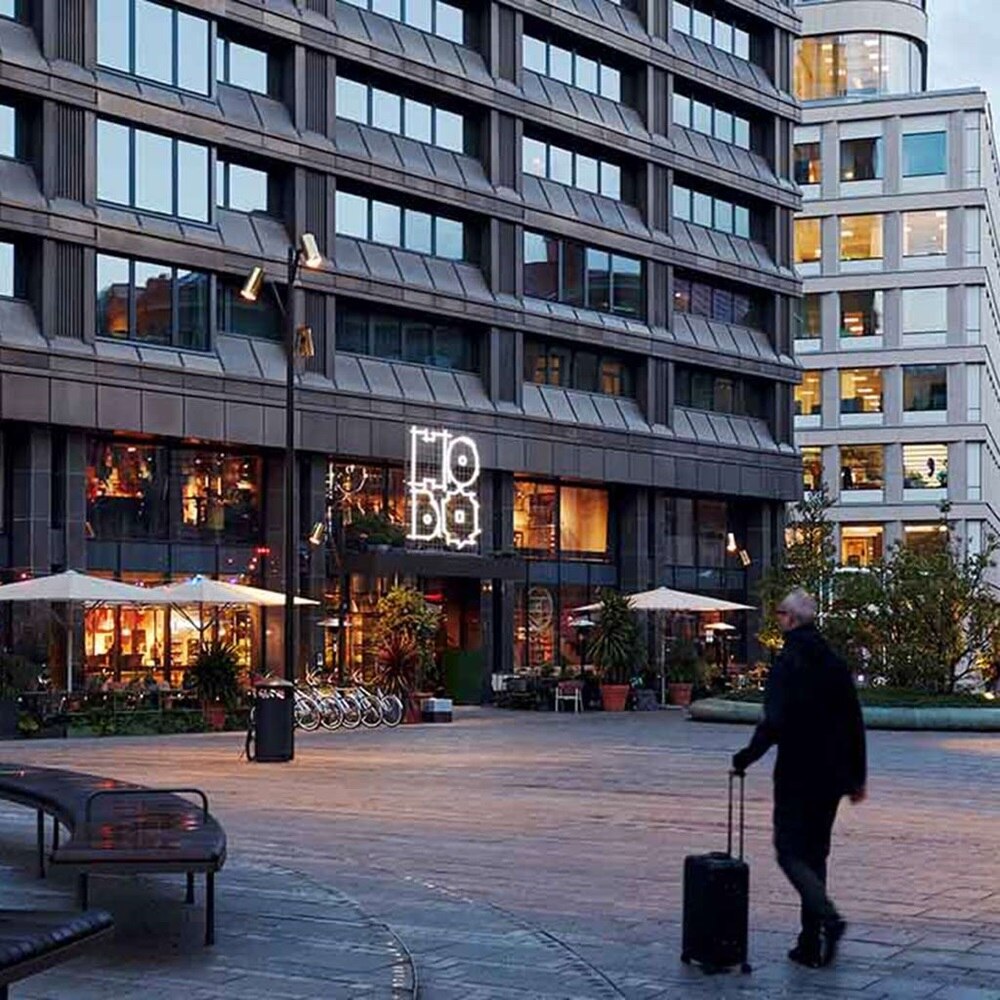 Bâtiments avec vitrines de magasin éclairées donnant sur une place piétonne.
