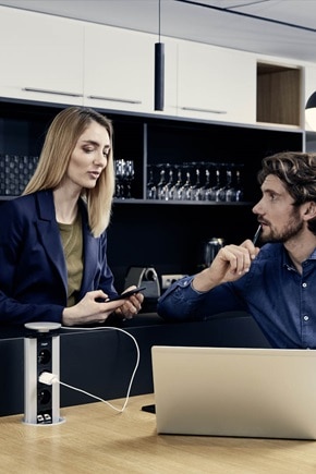 Homme avec un ordinateur qui échange avec une femme tenant son smartphone branché à une colonnette Hager