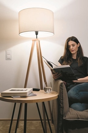 Femme dans un fauteuil qui lit un livre à côté d'une petite table et d'un lampadaire dont l'éclairage peut être actionné par l'interrupteur à proximité