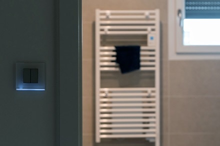 appareillage mural gallery de Hager, finition moon glass, fonction double va-et-vient équipé de la bande lumineuse, à l’entrée d’une salle de bain avec sèche-serviettes.