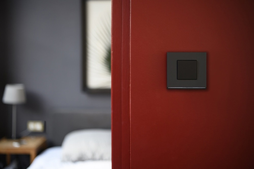 Interrupteur gallery de Hager finition night avec bande lumineuse sur un mur rouge à l'entrée d'une chambre dans les tons gris