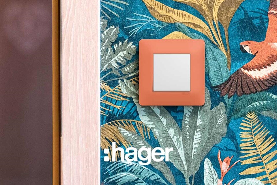 Interrupteur essensya de Hager, finition coral, sur un papier peint jungle luxuriante et perroquet