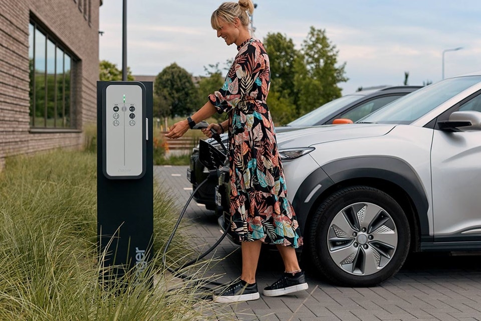 Borne de charge witty de Hager, femme rechargeant un véhicule électrique sur un parking