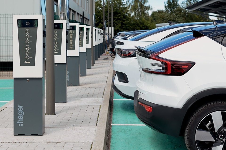 Flotte de véhicules électriques stationnées devant les bornes de recharge witty de Hager sur un parking d'entreprise
