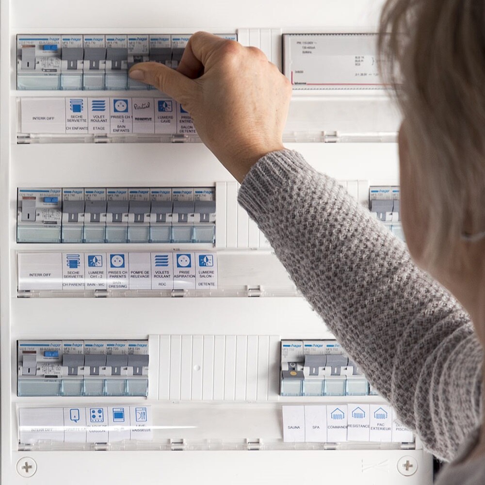 Femme qui réarme un disjoncteur dans un coffret gamma de Hager. L'installation répond aux exigences de la norme NF C 15-100.