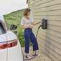 Femme qui charge son véhicule électrique avec une borne de recharge witty one de Hager posée sur le mur de sa maison
