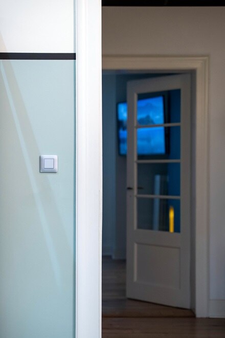 Appareillage mural essensya de Hager, finition titane, fonction va-et-vient titane sur mur bleu pastel dans couloir avec pièce en arrière-plan